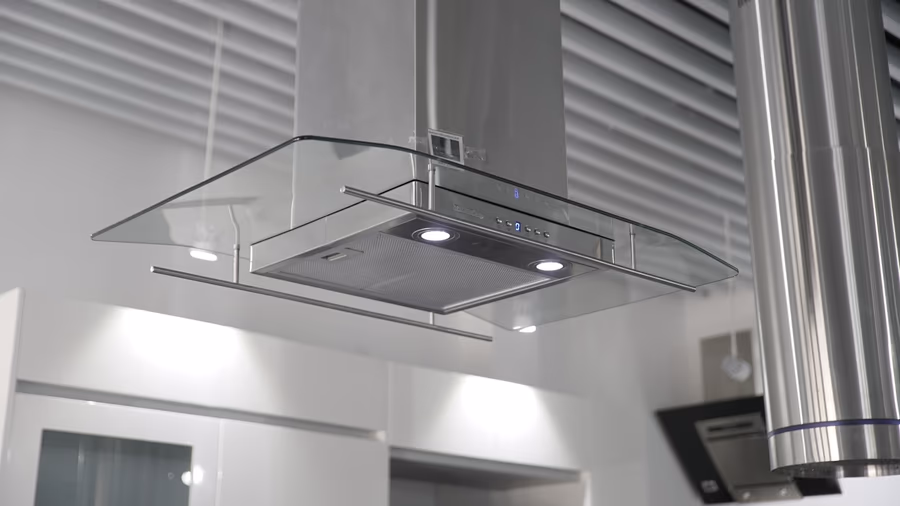 A glass and stainless island extraction hood suspended below a ceiling, with the circular duct rising from it into the ceiling